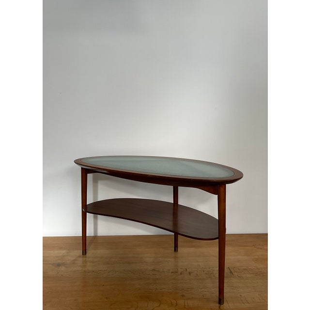 A beautiful mahogany and glass coffee table with brass feet. Kidney shaped top with raised edge and an underlying shelf....