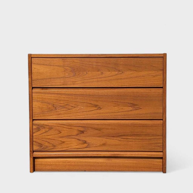 A compact teak three-drawer chest with expressive flowing grain, full-width integrated pulls and a recessed base. Its...