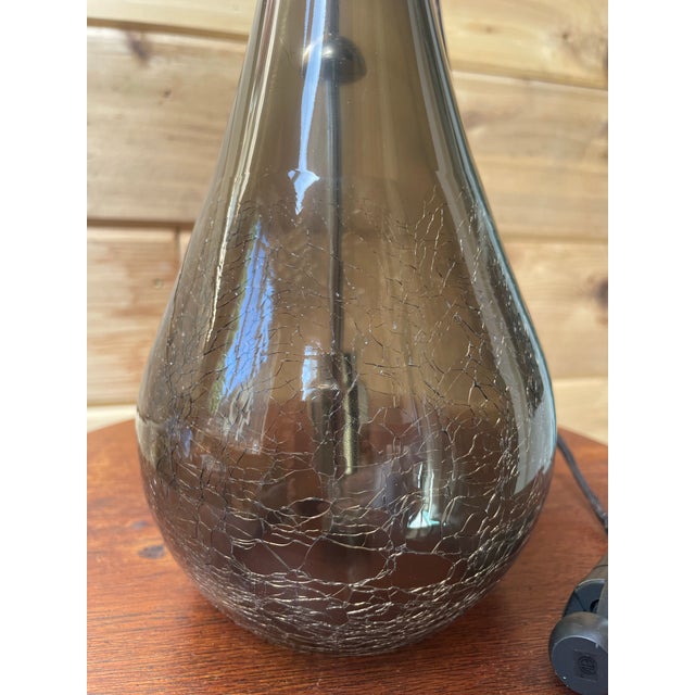 A striking hand-blown pendant crafted from smoke-tinted crackle glass with bronze hardware. The sculptural, elongated form...