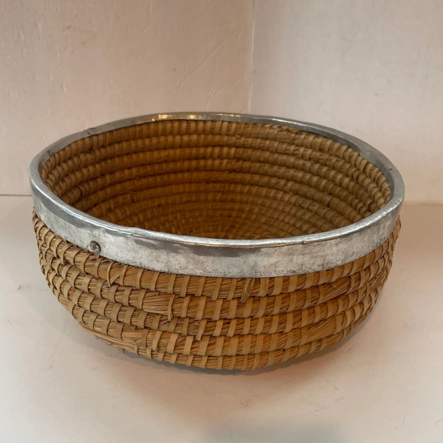 Handmade rustic coiled basket with metal band at the top. Measures 12" in diameter x 5" high. A lovely accent piece that...