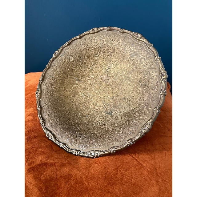 A richly detailed vintage brass pedestal bowl featuring an elaborate repoussé-style surface with a central floral...