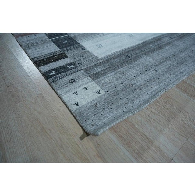 This gray wool rug features a hand knotted pile construction in the traditional Gabbeh style. Produced in India, it...