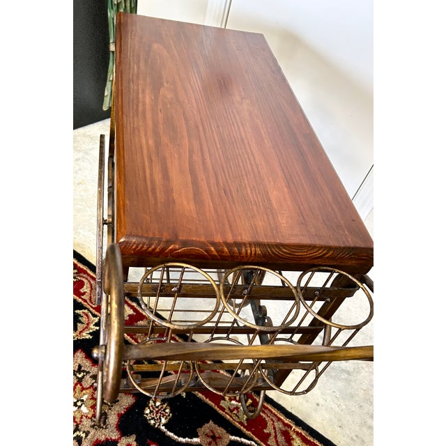 Offering a vintage weight iron and wood slab fancy trolley cart with wine storage. Wood top is pristine and wheels roll well.