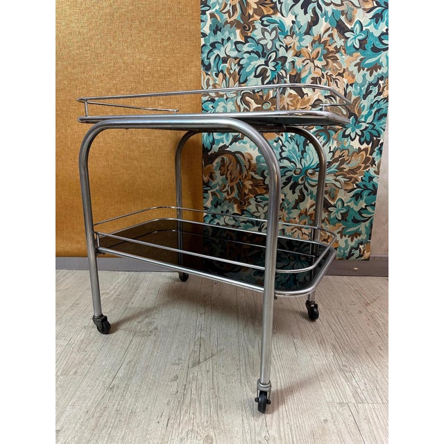Very beautiful art deco trolley on casters in chrome metal and two removable trays in black tinted glass. In the style of...
