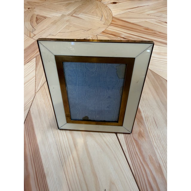 An elegant tabletop picture frame with a wide ivory-colored border, mitered corners, and a warm brass-tone inner trim. Its...