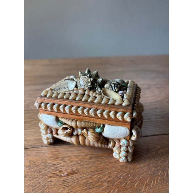 A petite treasure, sweetly scaled and full of coastal charm. This vintage English shell-covered trinket box carries...