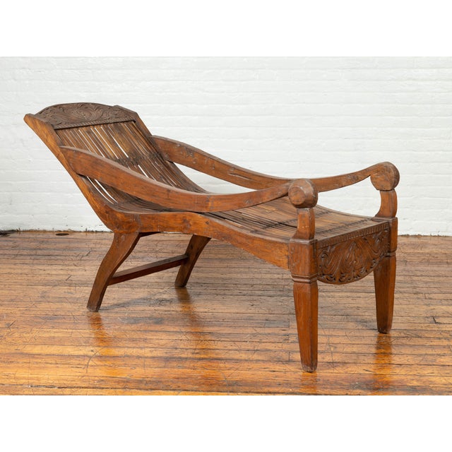 An antique Indonesian reclining plantation lounge chair with bamboo slats and carved motifs. Designed to provide a...