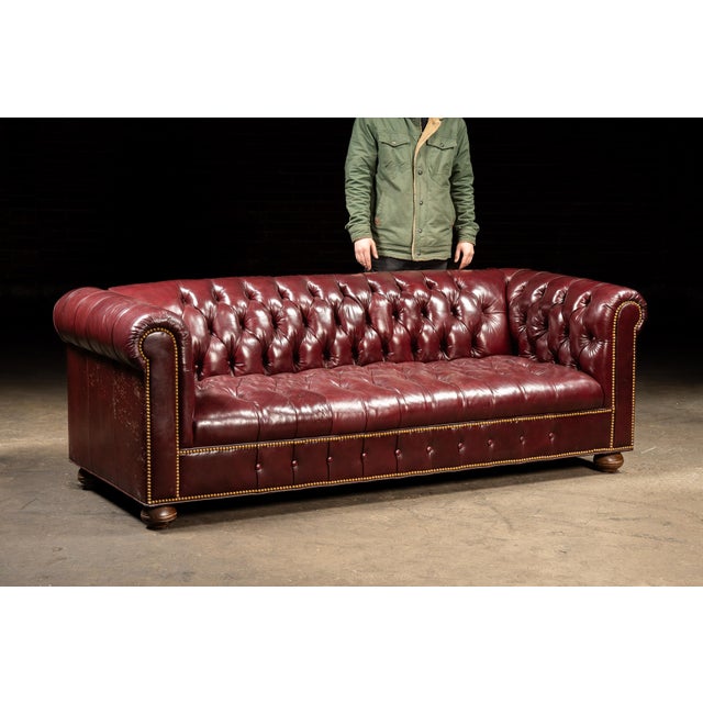 A handsome vintage Chesterfield sofa upholstered in deep red leather. Its substantial profile features a low back aligned...