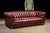 A handsome vintage Chesterfield sofa upholstered in deep red leather. Its substantial profile features a low back aligned...