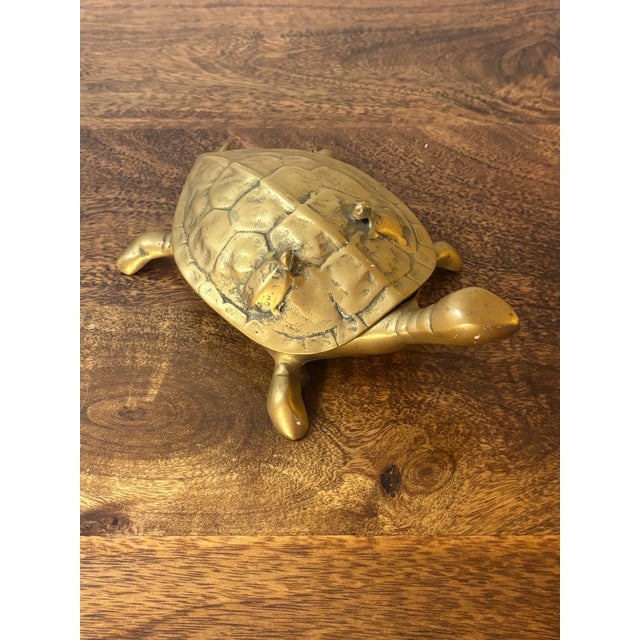 A whimsical vintage brass turtle dish featuring a hinged, lift-top shell that reveals a small trinket compartment. The...