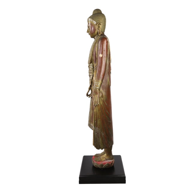 This Buddha statue is made of woodcarving, with gold foil and inlaid glass or semi-precious stones on the surface, showing...