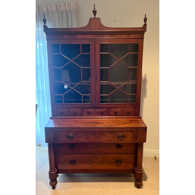 Early 1900s flame mahogany secretary featuring an upper bookcase with mullioned doors, adjustable shelving, pen and pencil...