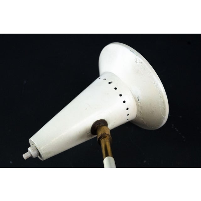 This elegant wall light features a conical shade mounted on a jointed structure with an adjustable arm, allowing the light...