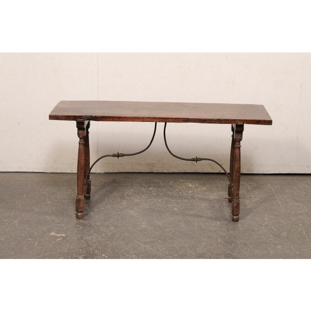 An Italian low-profile carved wood trestle-leg table, with forged-iron stretcher, from the 18th century. This antique...