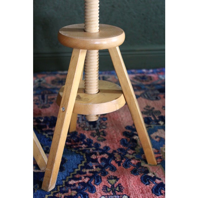A pair of adjustable artist stools blonde wood with angular legs and exposed screw mechanisms. Each stool easily raises or...