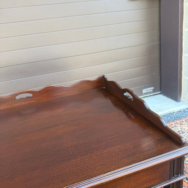 A vintage Chippendale mahogany butler's tray coffee table having a fixed top with scalloped gallery over fluted block legs...