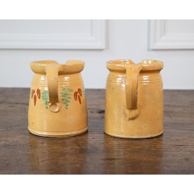 Charming 19th-century French terracotta pottery pitchers, each featuring a warm ochre-yellow glazed finish and hand-...