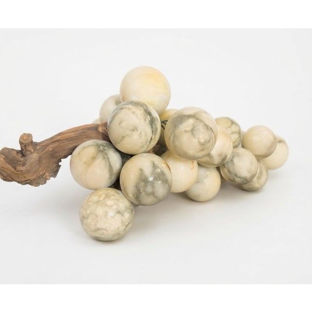 A substantial vintage marble grape-cluster sculpture resting on a beautifully textured natural grapevine branch. The...
