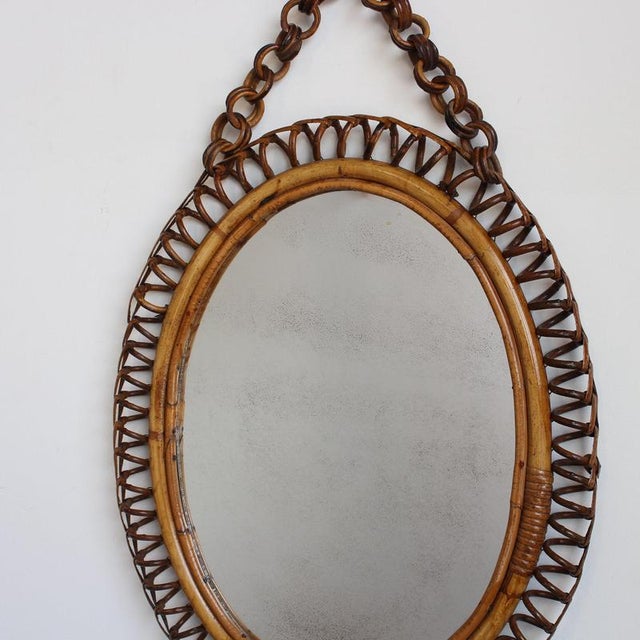 Italian oval-shaped rattan wall mirror (circa 1960s). This mirror has a very charming shape with rattan spirals framing...