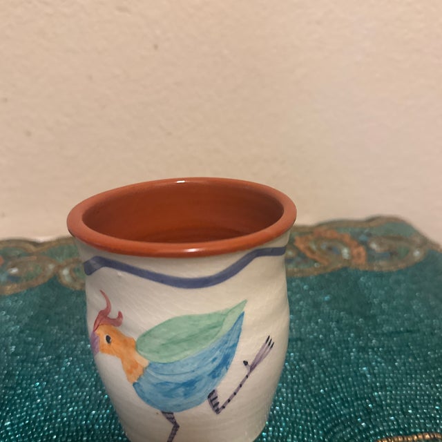 A hand-painted ceramic pencil holder featuring a whimsical, multicolored bird illustration against a cream-white...