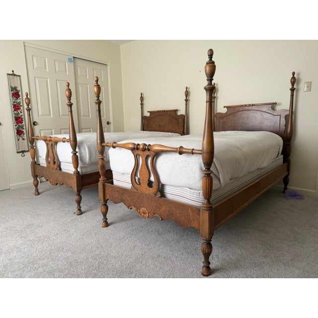 A pair of twin sized four poster beds featuring carved wooden headboards with scrollwork and urn finials, low footboards...