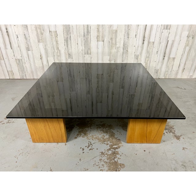 Over-sized smoked glass with L shaped wood legs make this cocktail tables a stunning addition to any room .