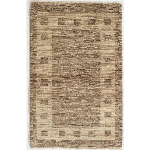Hand-knotted Gabbeh wool rug featuring a soft striated field in beige and brown tones with a subtle geometric border....