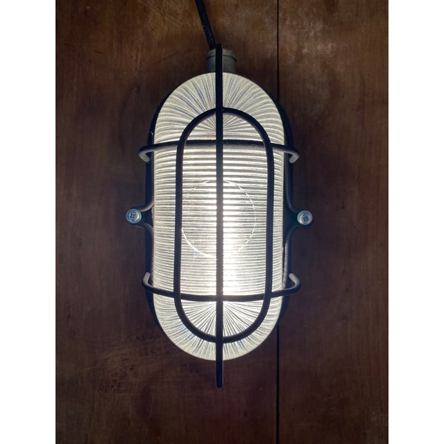 Vintage industrial bulkhead light featuring a robust cast metal housing, protective steel cage and original ribbed...