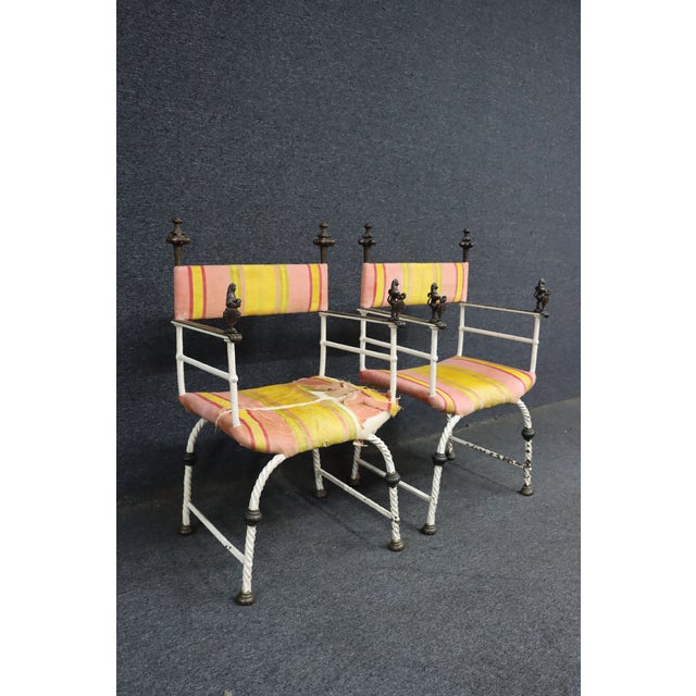 Pair of Italian Savonarola-style chairs featuring iron frames with bronze-tone figural arm details. The arms are accented...