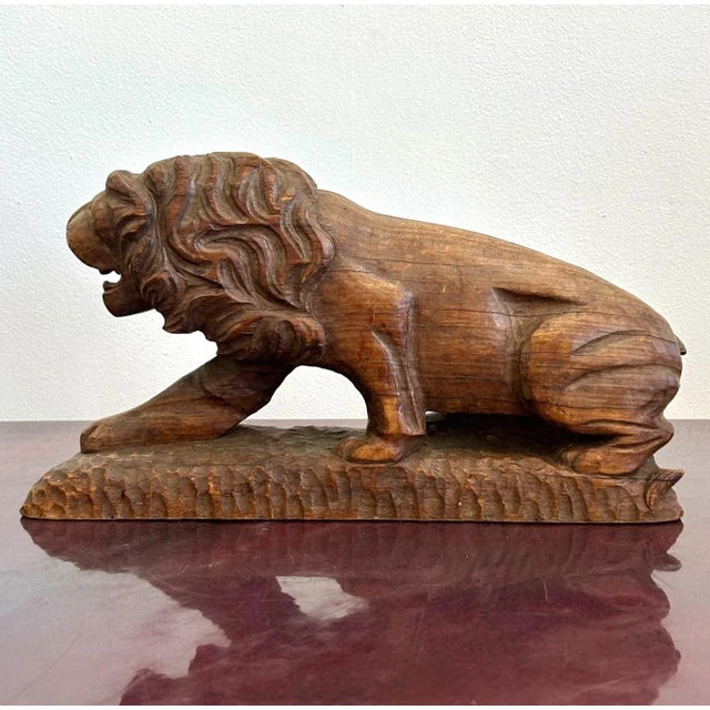 This hand-carved wooden sculpture depicts a lion in a crouched, powerful stance, with one paw extended forward and its...