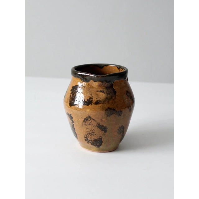 Vintage signed studio pottery pitcher featuring a hand-crafted ceramic form with a striking black and tan glaze. The...