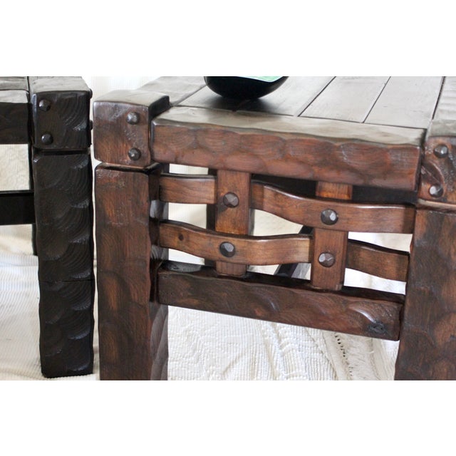 A pair of substantial pine tables in a rustic or Brutalist style with details of faceted wood, grommets, dark stain, and...