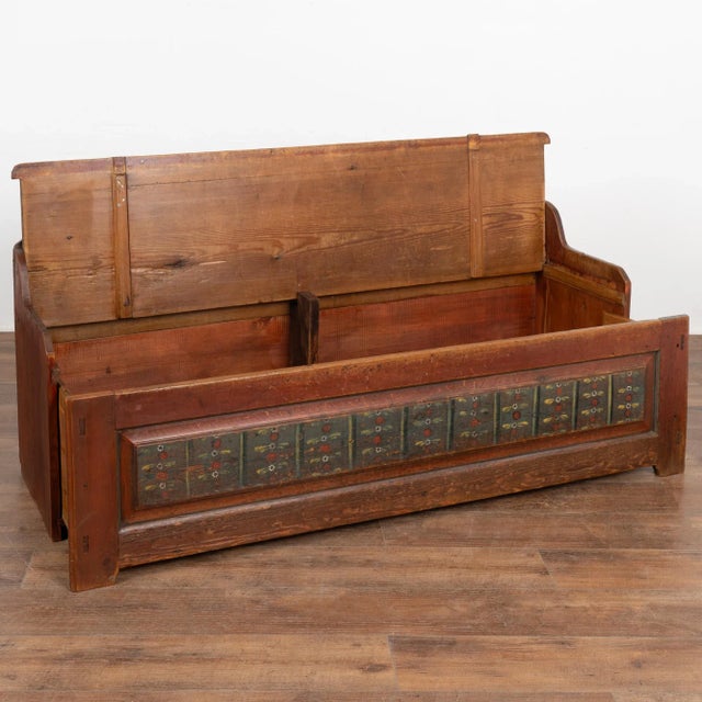 Original hand painted pine bench displays a brick red/brown background and simple folk art motif along the front panel....