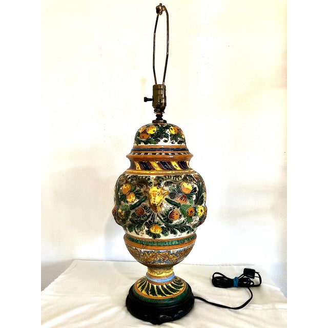 This vintage Italian ceramic table lamp features a colorful, hand-painted design with green foliage framing floral and...