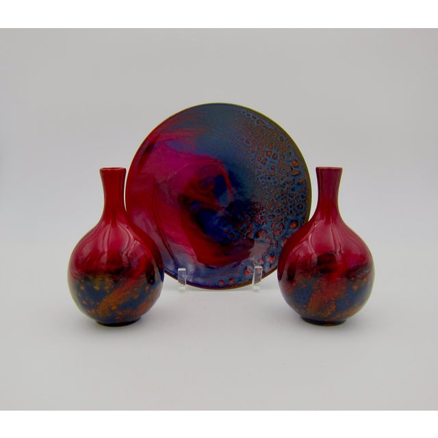 A trio of English veined flambé art pottery objects consisting of a round shallow dish with a pair of matching cabinet...