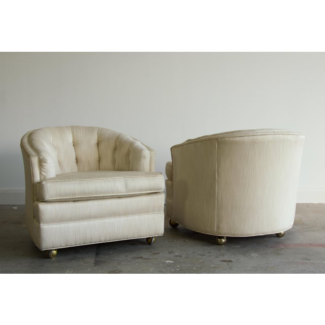 A pair of vintage club chairs with a curved barrel back, channel tufting, and self-covered buttons. The rolled crest and...