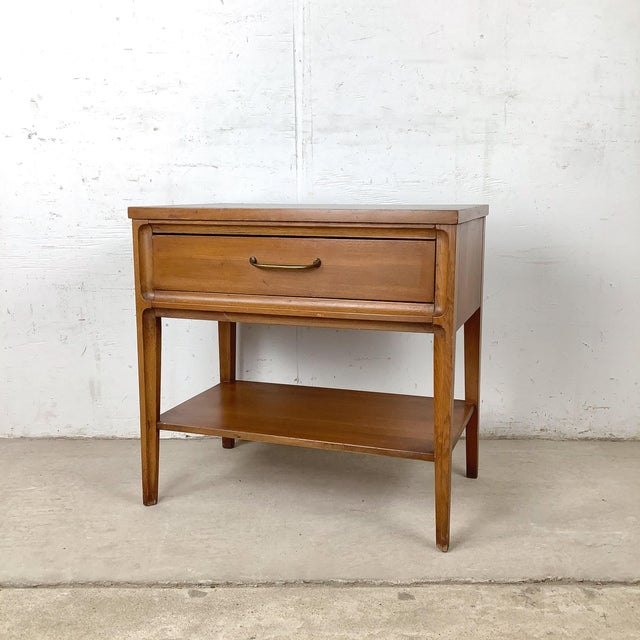 This vintage mid-century nightstand features a classic American modern form with a black top, single drawer, and open...
