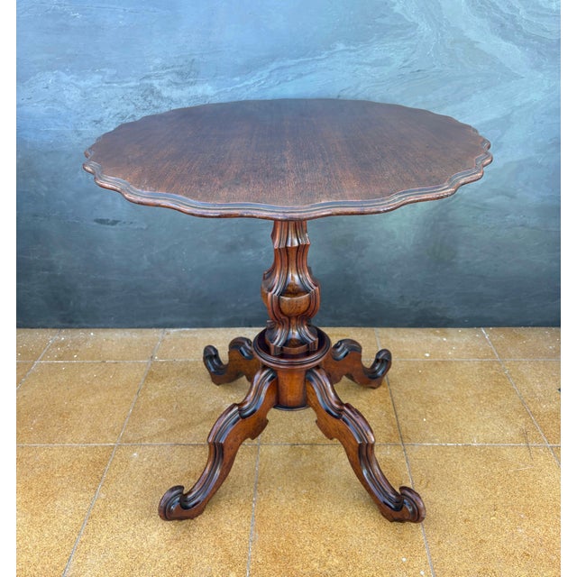 20th-century Victorian tilt-top pedestal table featuring a rotating circular top with a finely scalloped edge. The table...