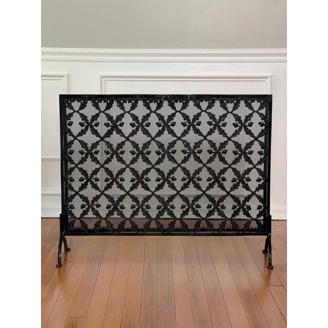 Offering an Arts and Crafts cast brass and iron single panel fire screen with a lattice design of oak leaf garlands and...