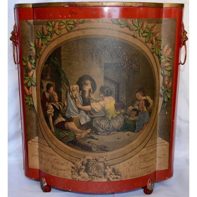 A vibrant red adorns this midcentury tin waste basket. It is embellished with a decoupage print depicting what appears to...