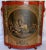 A vibrant red adorns this midcentury tin waste basket. It is embellished with a decoupage print depicting what appears to...