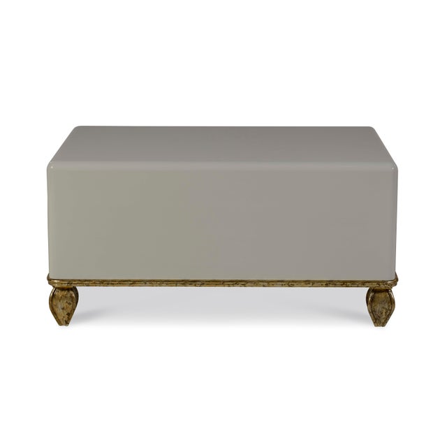 The contemporary high gloss light grey lacquered ottoman coffee table featuring mid-century inspired feet, showcases a...