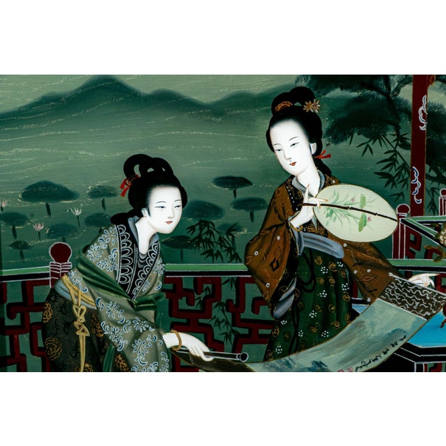 A finely hand-painted Chinese reverse painting on glass depicting two elegant court ladies examining a painted hand scroll...