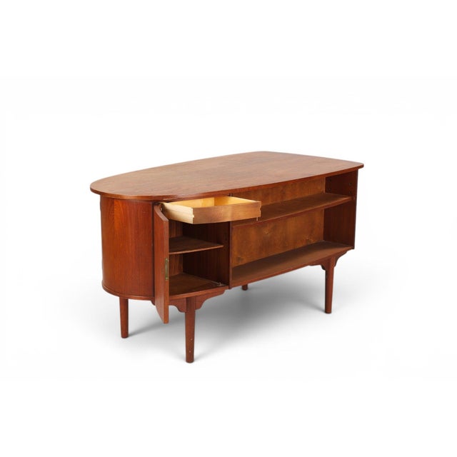 A striking atomic-era "bullet" writing desk in teak, named for its torpedo-like silhouette and sculpted, tapering legs....