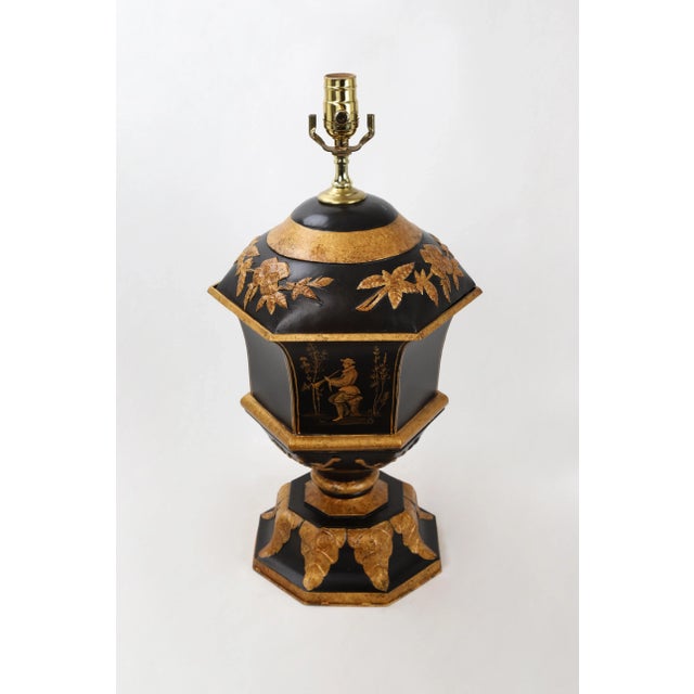 Vintage tole trophy lamp, painted in black and gold color. Leaf reliefs adorn the top and bottom of the lamp, and a man...