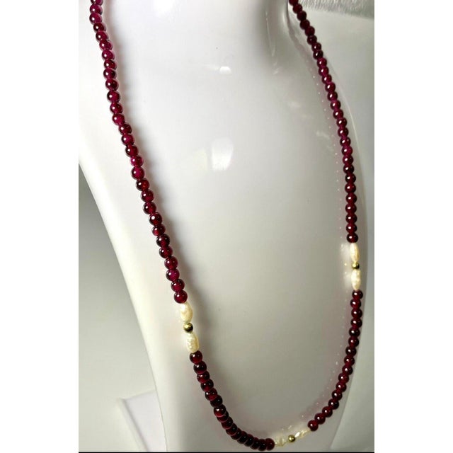 A 14k gold necklace with Rhodolite garnet that exhibits distinct pinkish-violet color tone, similar to ruby. Accompanied...