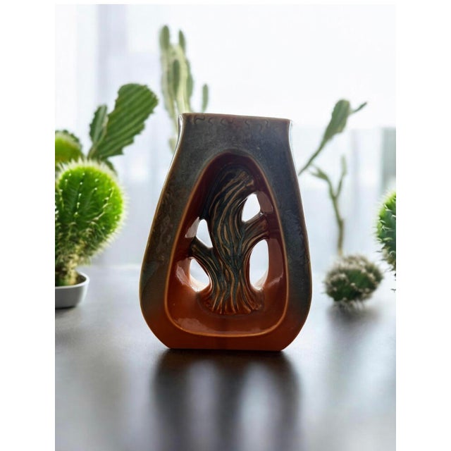 This vase's design features a tree trunk motif within an open cutout. The combination of earthy tones and the stylized...