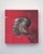This artwork features a striking depiction of a metallic helmet, rendered in rich oil paint against a vibrant red...