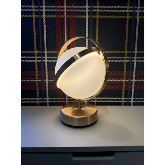 Brass finish table lamp consisting of a frosted glass globe surrounded by two concentric rings. The globe is illuminated...
