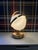 Brass finish table lamp consisting of a frosted glass globe surrounded by two concentric rings. The globe is illuminated...